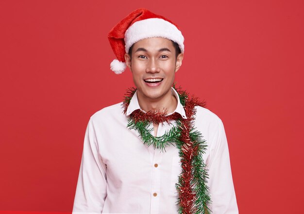 赤で隔離のクリスマスパーティーオフィスでサンタの帽子をかぶってアジアのビジネスマンを笑顔