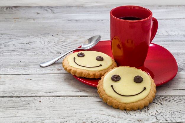 一杯のコーヒー、木製の背景、食品と赤いプレートにクッキーを笑顔します。