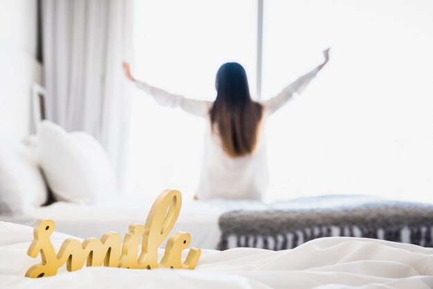 Smile word on white blanket with woman stretching her hands at backdrop