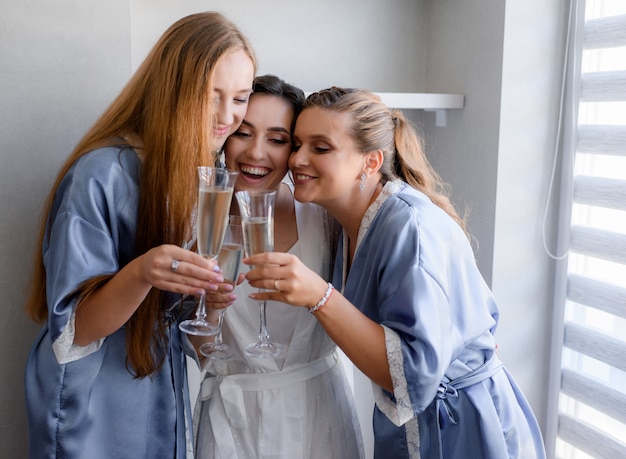 Улыбающиеся подружки невесты, одетые в синюю шелковую ночную одежду, и невеста пьют шампанское в комнате