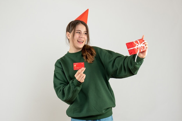 Sorrise ragazza con tappo del partito che tiene regalo e carta su bianco