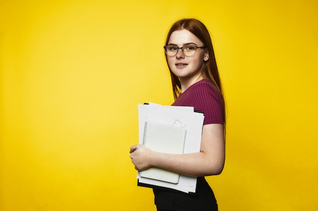 Smiled redhead caucasian girl is holding notebooks and files in hands