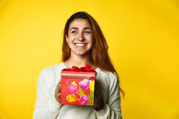 Smiled redhead caucasian girl is holding red present in hands with excited face