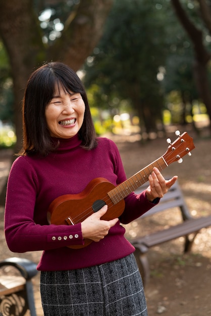 Donna asiatica sorridente che suona ukulele a colpo medio