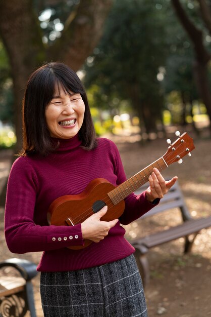 Smiley asian woman playing ukulele medium shot