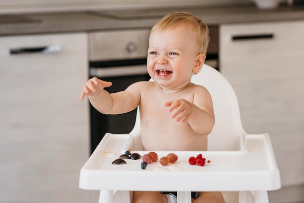 Smiley baby in highchair choosing what fruit to eat