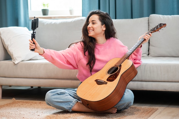 Free photo smiley blogger smiling and recording herself with her guitar