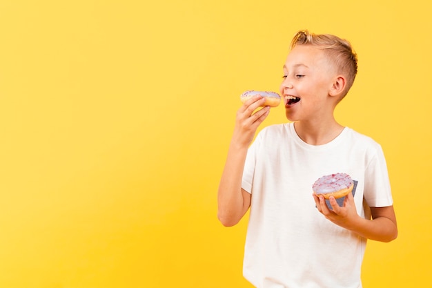 Foto gratuita ragazzo di smiley che mangia ciambella deliziosa