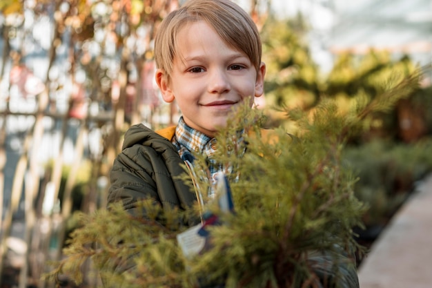 Free photo smiley boy holding a small tree in a pot