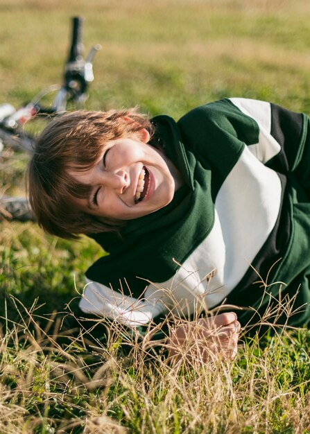 Smiley boy relaxing on grass while riding his bike