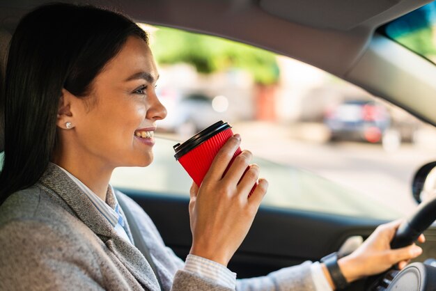 Smiley businesswoman driving and having coffee