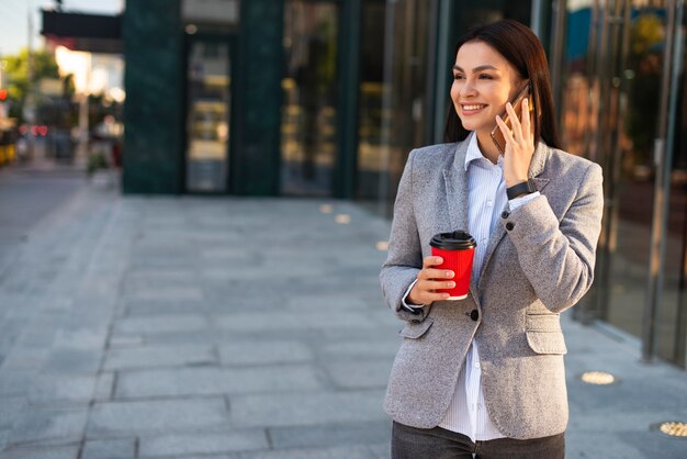 Donna di affari di smiley che parla sul telefono mentre beve caffè con lo spazio della copia