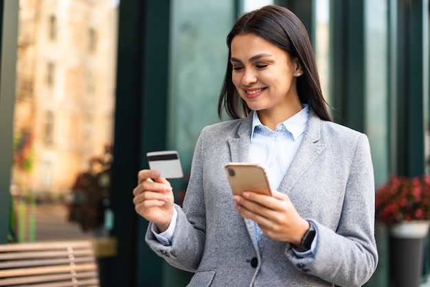 Free photo smiley businesswoman using smartphone and credit card outdoors