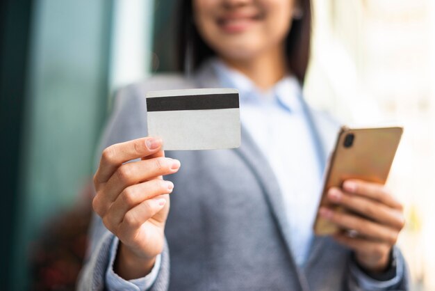 Смайлик бизнесвумен со смартфоном и кредитной картой на открытом воздухе