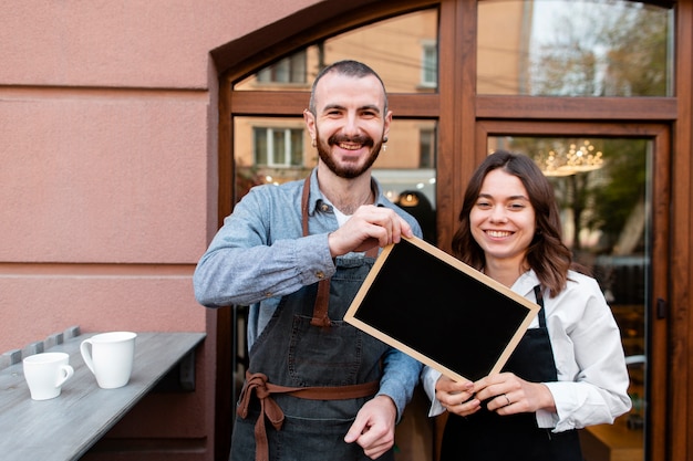 Free photo smiley coffee shop owners holding frame