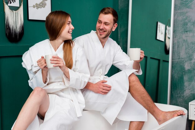 Smiley couple in bathrobes holding cups