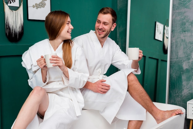 Smiley couple in bathrobes holding cups