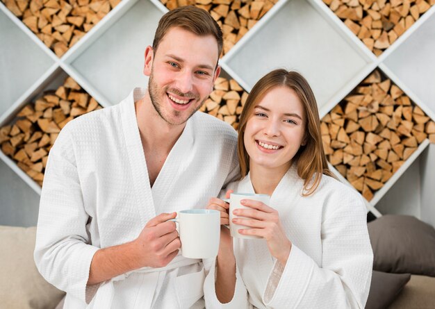 Smiley couple in bathrobes posing with cups