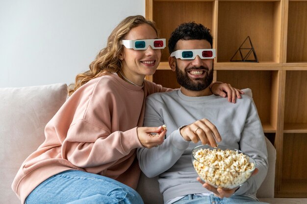 팝콘을 먹고 3 차원 안경으로 집에서 영화를 보는 웃는 커플
