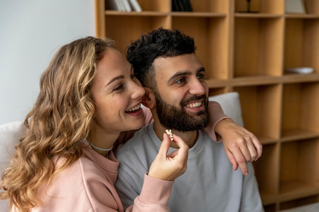 Free photo smiley couple eating popcorn and watching movie at home