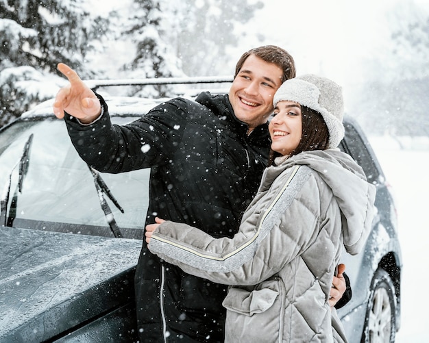 Smiley couple embracing in the snow while on a road trip