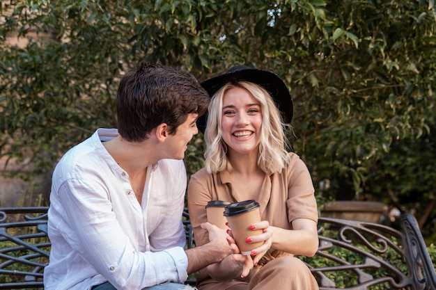 Free photo smiley couple enjoying coffee on the bench