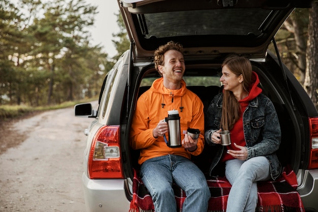 車のトランクで温かい飲み物を楽しんでいるスマイリーカップル