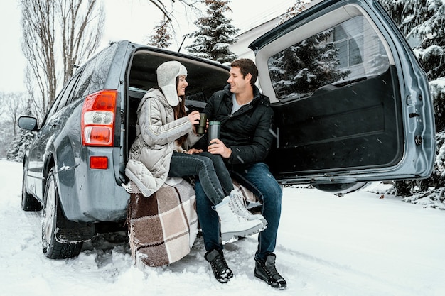 Улыбающаяся пара с теплым напитком в багажнике машины во время поездки