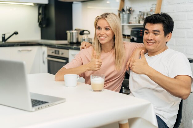 Smiley couple at home during the pandemic giving thumbs up while looking at laptop