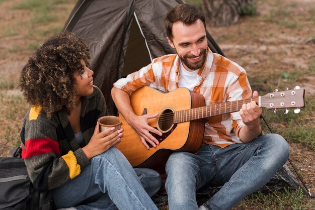 Smiley couple playing guitar while camping outside