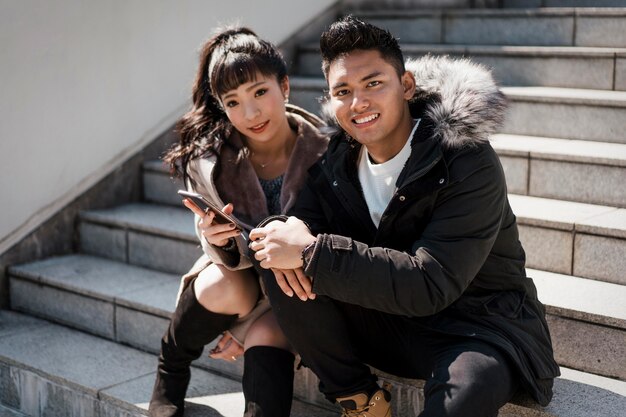 Smiley couple sitting on stairs with smartphone