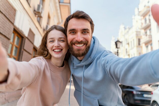 街の屋外で一緒に自分撮りをしているスマイリーカップル