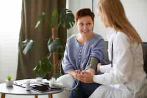 Free photo smiley covid recovery center female doctor checking elder patient's blood pressure