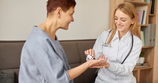 Free photo smiley covid recovery center female doctor giving elder patient pills