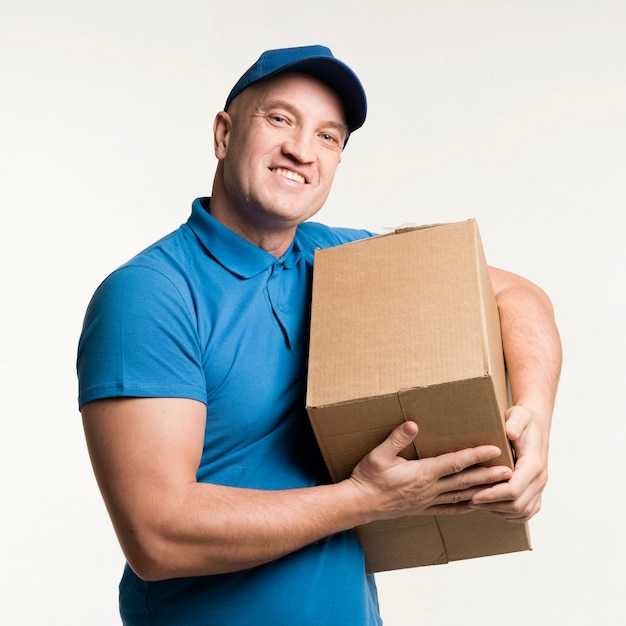 Smiley delivery man holding cardboard box in arms