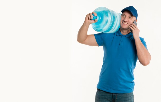 Smiley delivery man holding smartphone and carrying water bottle