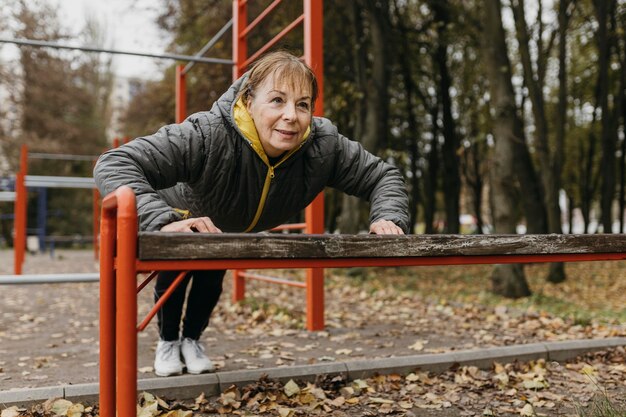 Смайлик старшая женщина делает отжимания на открытом воздухе