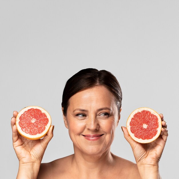 Смайлик старшая женщина держит половину грейпфрута в каждой руке