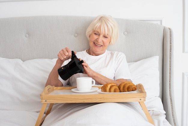 Улыбающаяся старшая женщина держит чайник в спальне