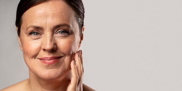 Smiley elder woman with make-up on posing with hand on face and copy space