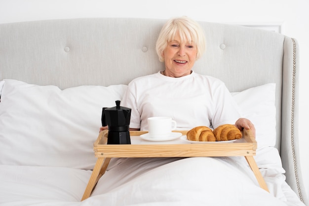 Smiley elder woman with tray in the bedroom