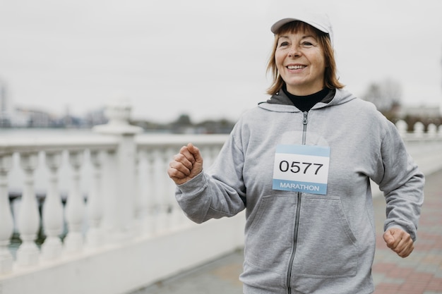 Free photo smiley elderly woman jogging outdoors with copy space