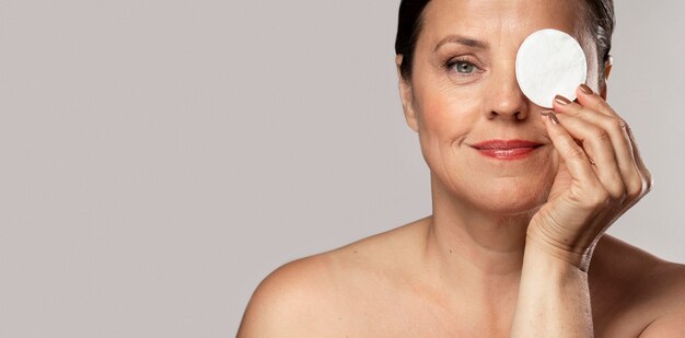 Smiley elderly woman posing with cotton pad for make-up removal and copy space