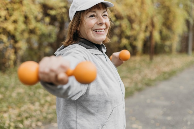 Smiley elderly woman working out with weights outdoors