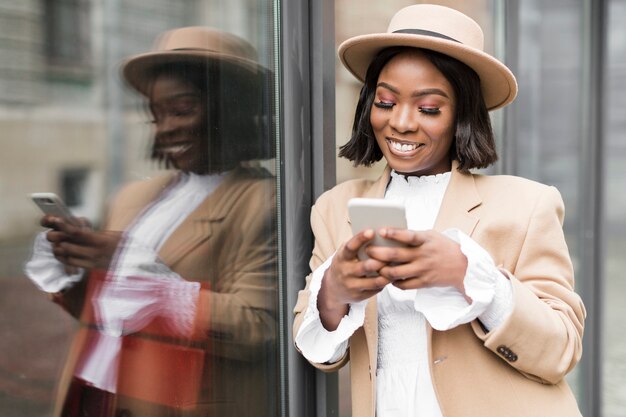 彼女の電話で見ているスマイリーのファッショナブルな女性