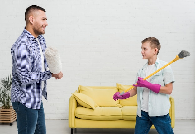 Smiley father and son play fight with duster and broom