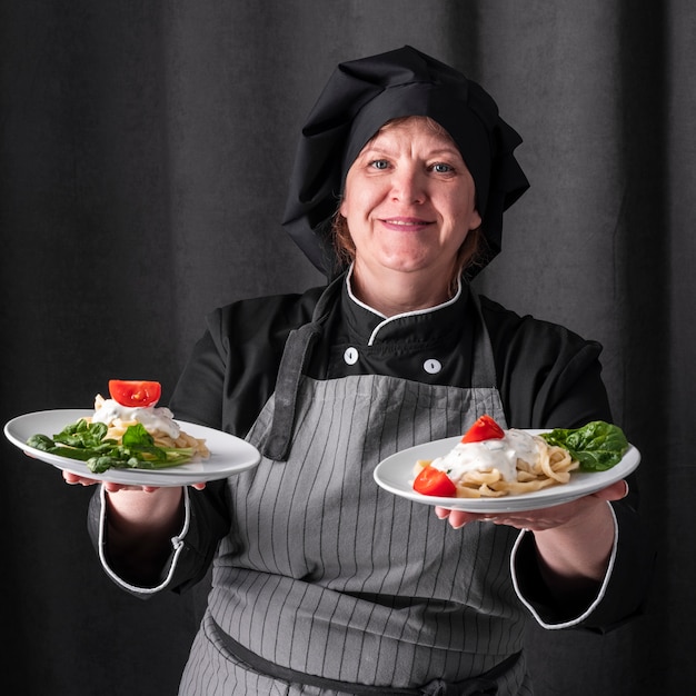 Free photo smiley female chef holding dishes in both hands