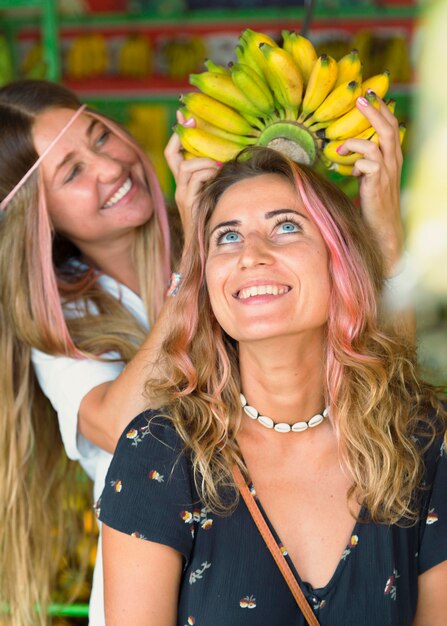 Smiley female friends at the farmers market fooling around with bananas