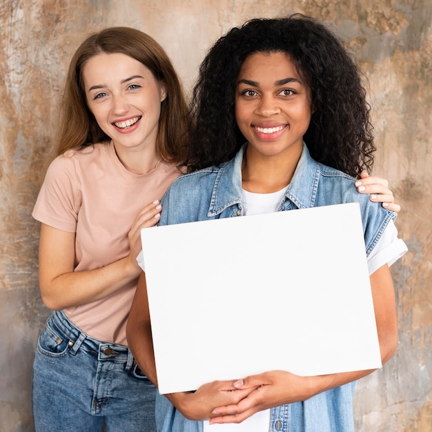 Free photo smiley female friends posing together while holding blank placard