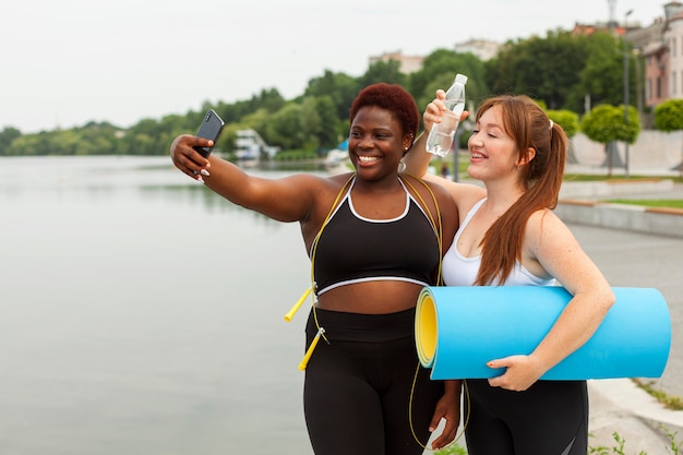 Smiley female friends taking selfie while exercising outdoors